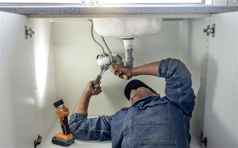 Plumber repairing pipes beneath a bathroom sink in Kennesaw