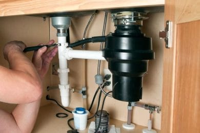 Plumber repairing a garbage disposal beneath a kitchen sink in Kennesaw
