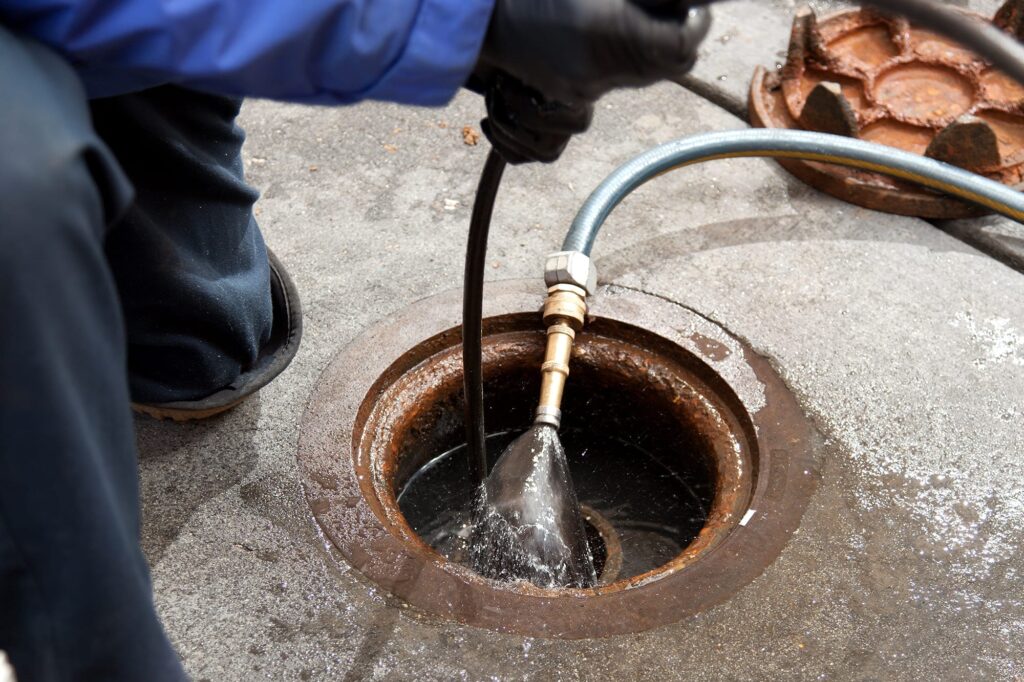 Plumber hydro jetting a sewer line through a manhole in Kennesaw