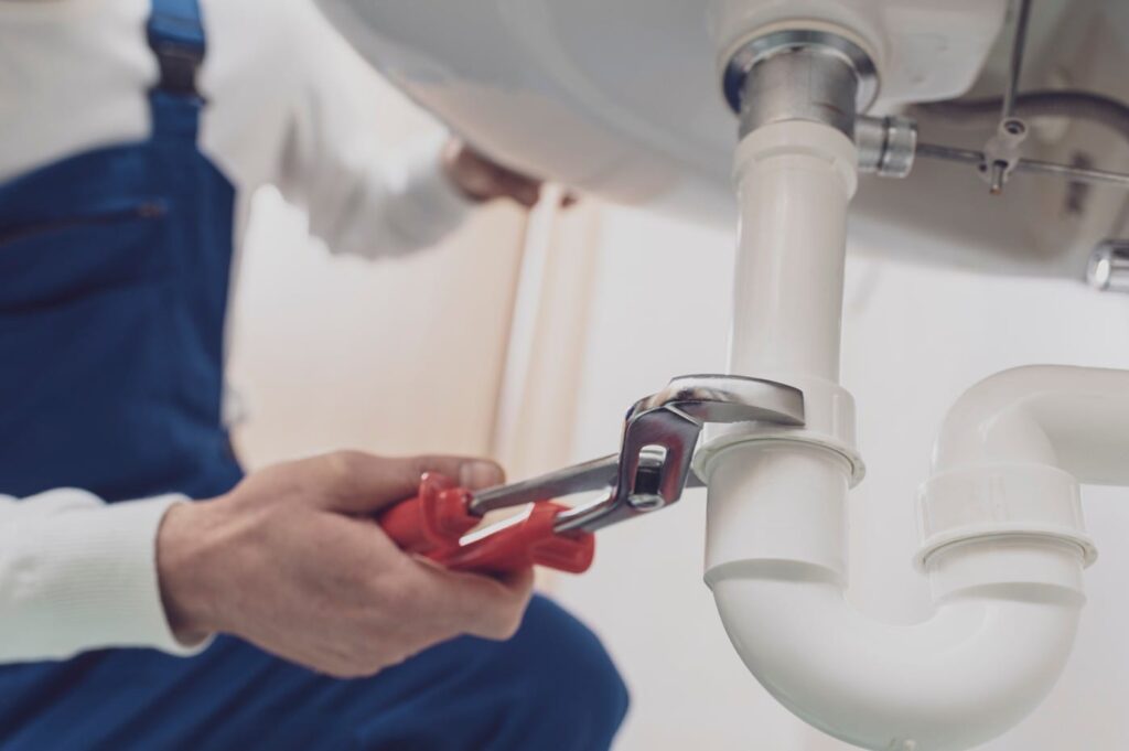 Plumber repairing a white drain pipe beneath a sink in Kennesaw