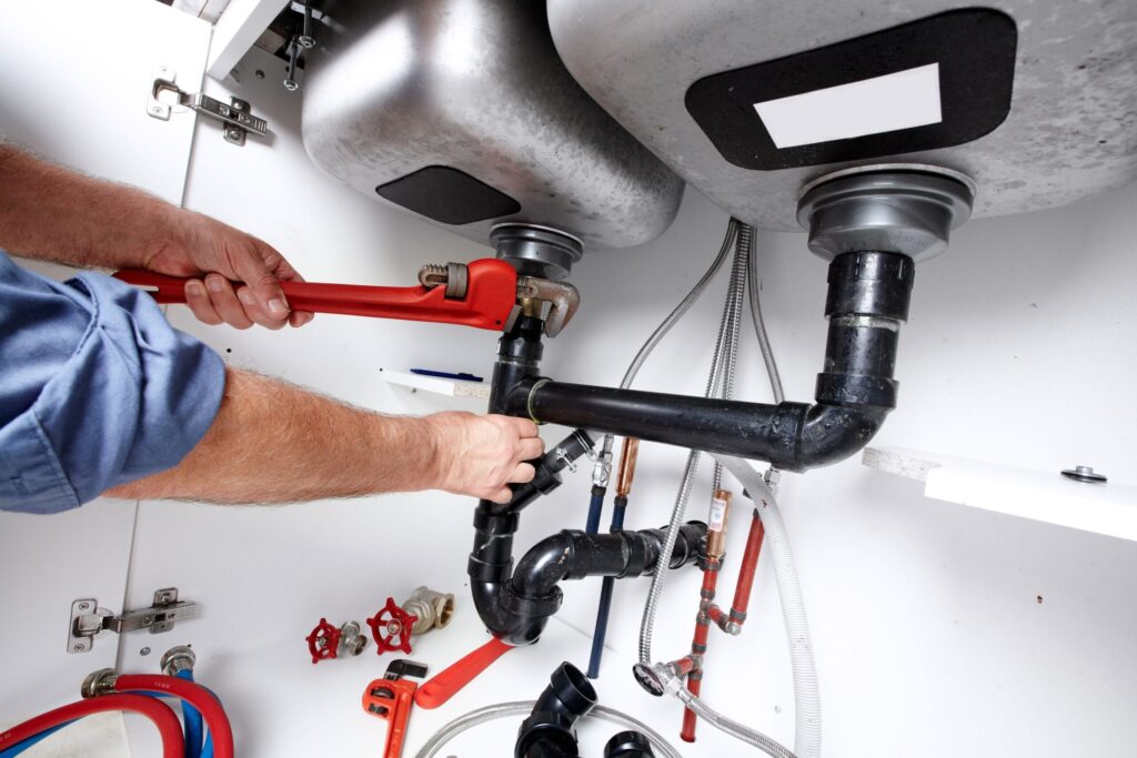 Plumber repairing drain pipes beneath a kitchen sink in Kennesaw